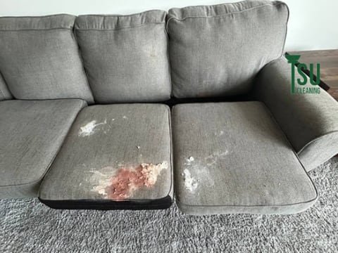 Grey three-seat sofa before cleaning, with a dark red stain across the seat cushion